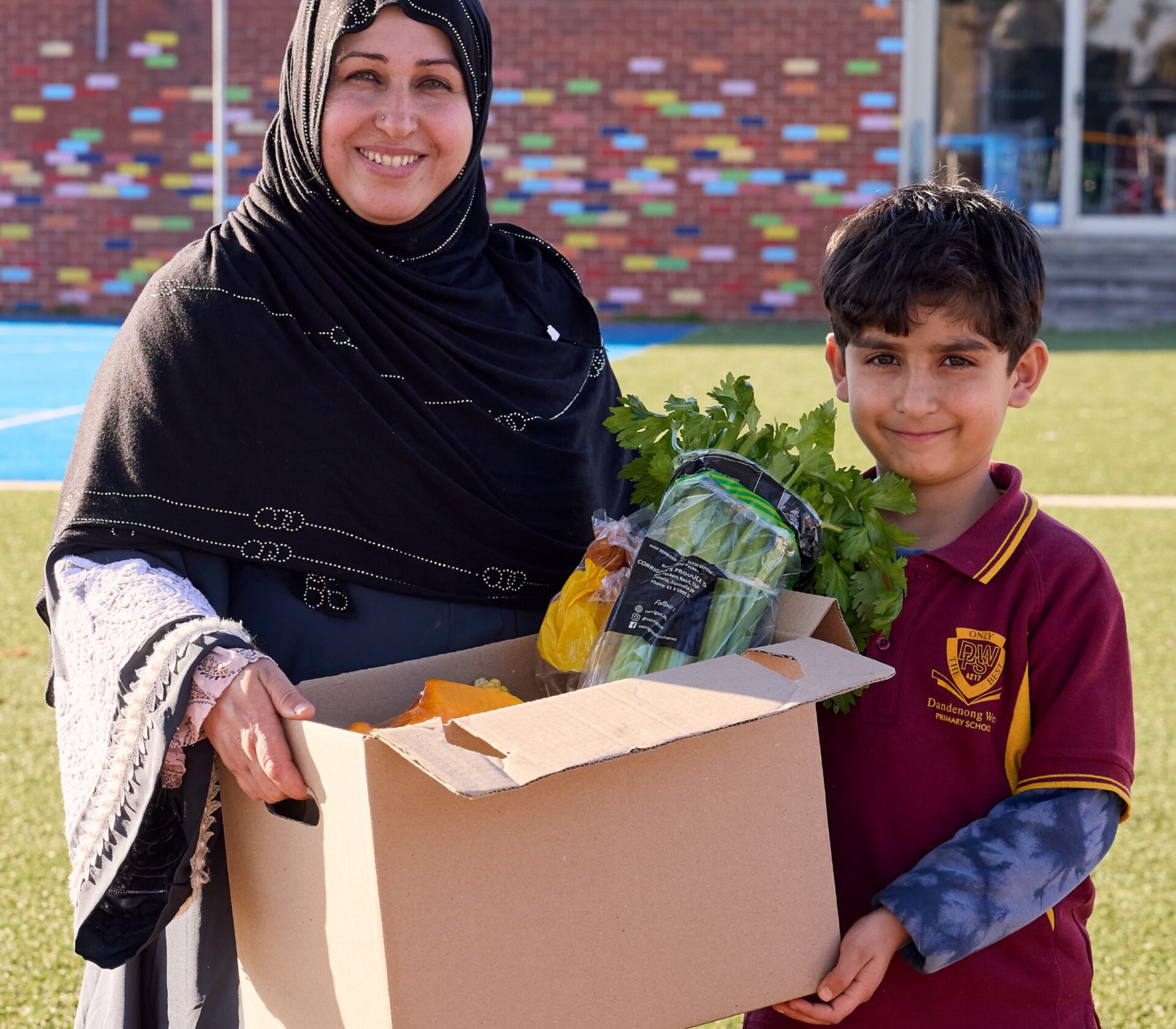 A mother and son carrying a box of fresh produce at school