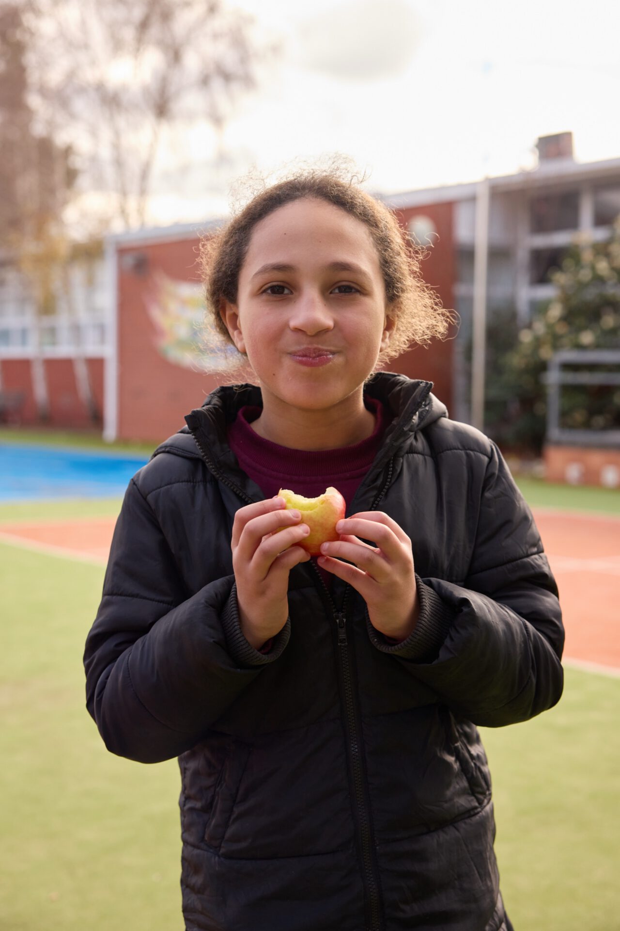 A schoolgirl smiling while eating an apple in the schoolyard