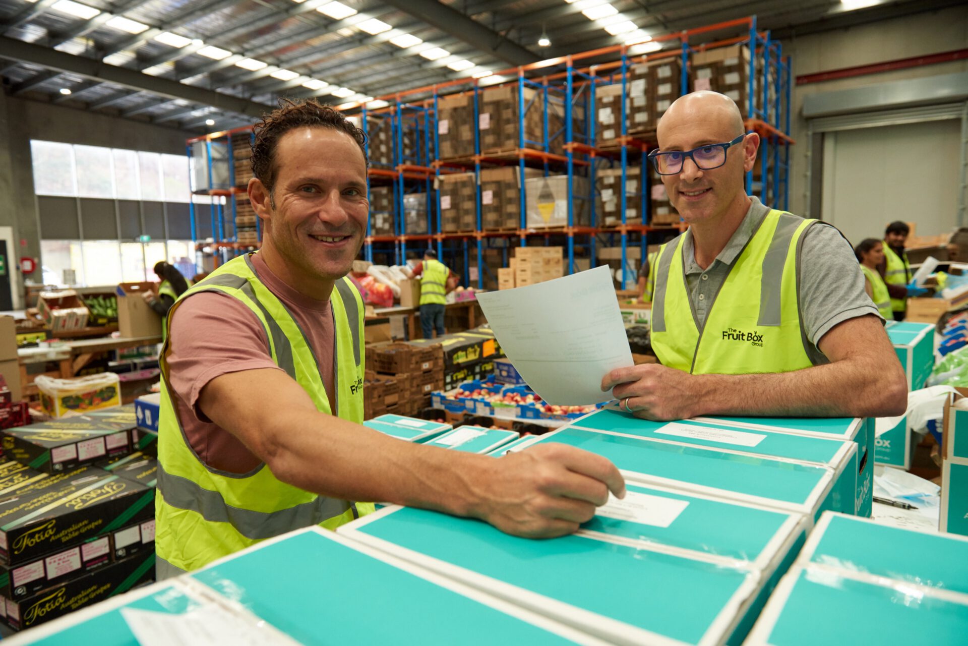 Two Fruit Box team members packing fresh food boxes in the warehouse