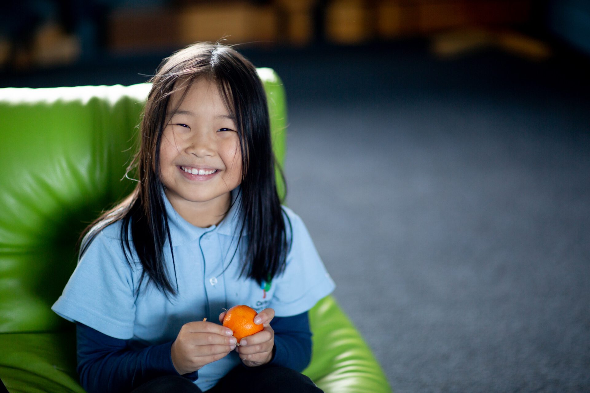 A young girl smiling and holding an orange