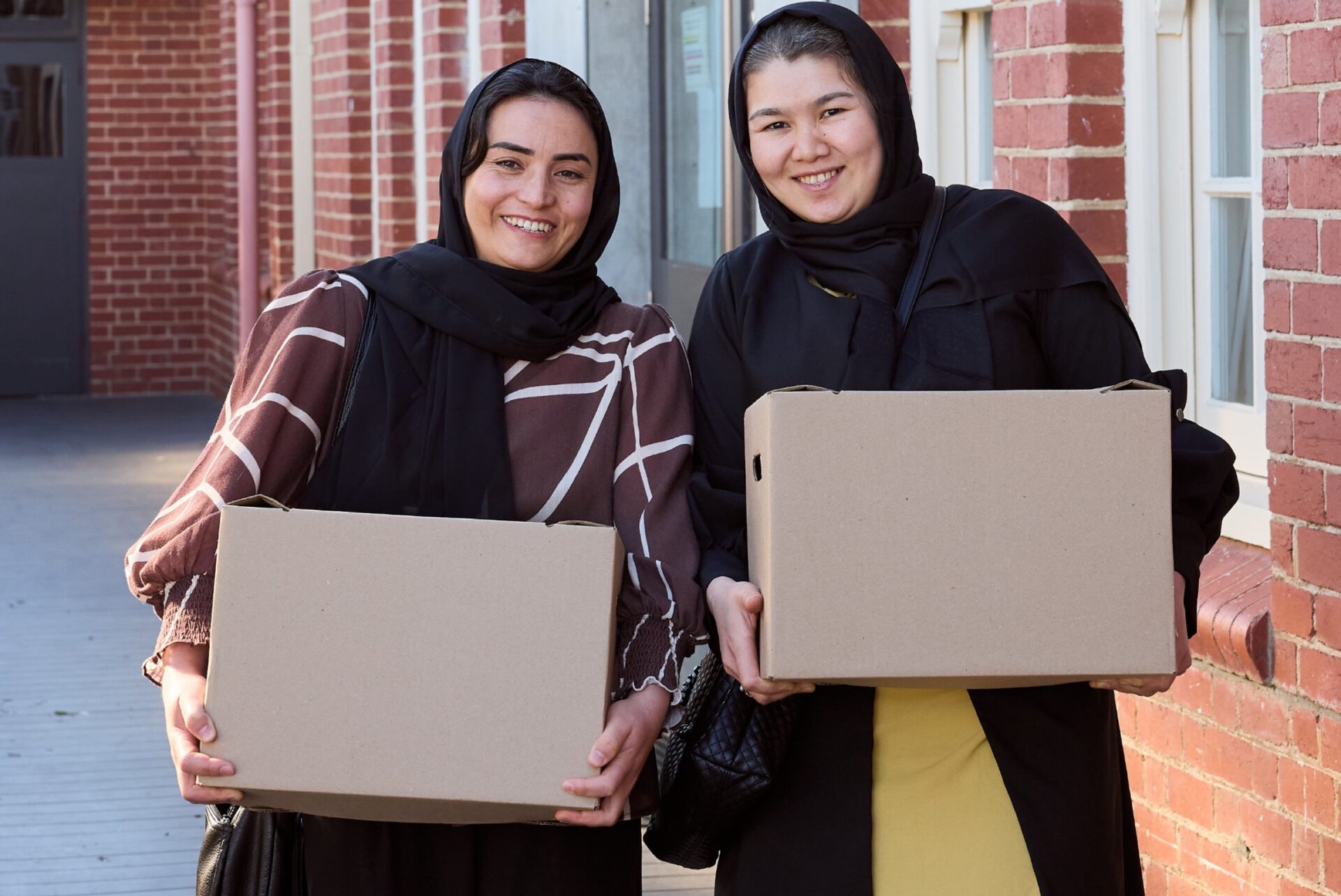 Two women carrying One Box boxes outside a school