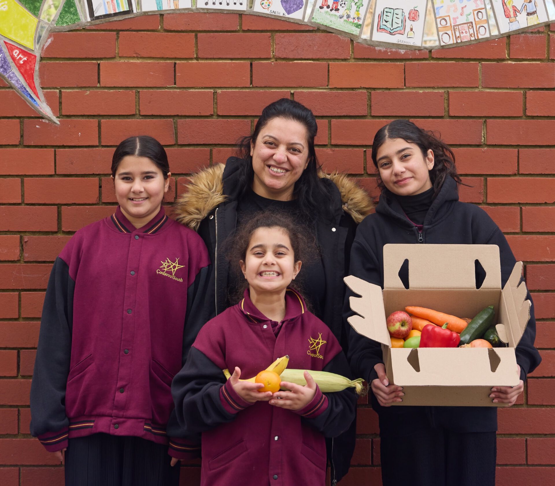 A mother and three daughters with a fresh produce box at school